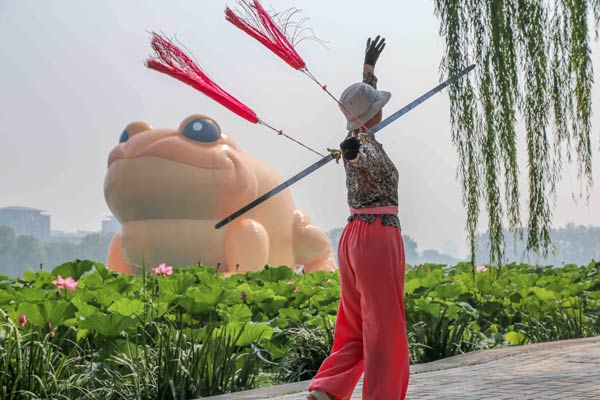 Una mujer practica un arte marcial chino frente a un sapo dorado inflable que flota en el lago del parque Yuyuantan de Pekín desde el 19 de julio. La presencia del sapo flotante ha abierto un debate en internet entre partidarios y opositores.