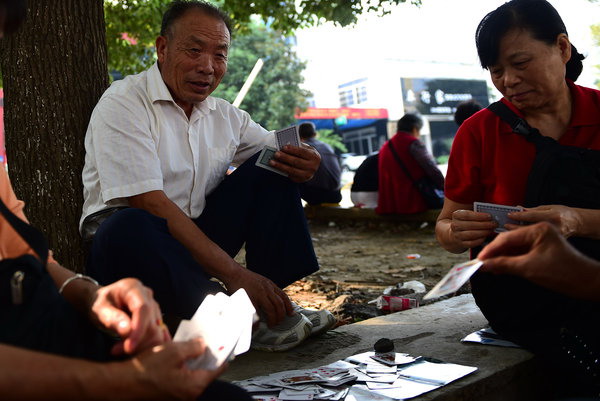 Kong Xianghai (izquierda), de 73 años, juega a las cartas mientras espera la salida del colegio de su nieto. después de jubilarse, Kong tiene dos ocupaciones principales: cuidar a su nieto y bailar en la plaza. [Foto: PPC]
