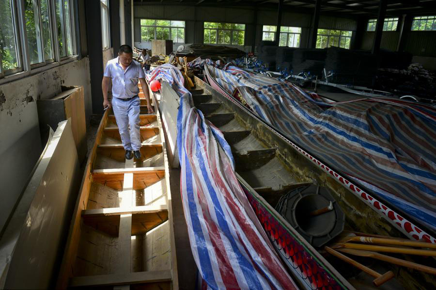 Peng camina sobre los barcos de madera fabricados por él en la ciudad de Chengdu, provincia de Sichuan, el 12 de junio de 2015. Como casi todos los barcos de dragón ahora están hechos de plástico reforzado con fibra, los barcos de madera hechos por Peng se amontonan en un almacén. 