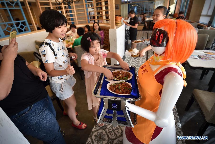 Una chica coge el plato que le entrega la camarera robot en Haikou, capital de la provincia de Hainan, el 3 de agosto de 2015. La camarerao robot trabaja en un restaurante de Haikou. [Foto/Xinhua]