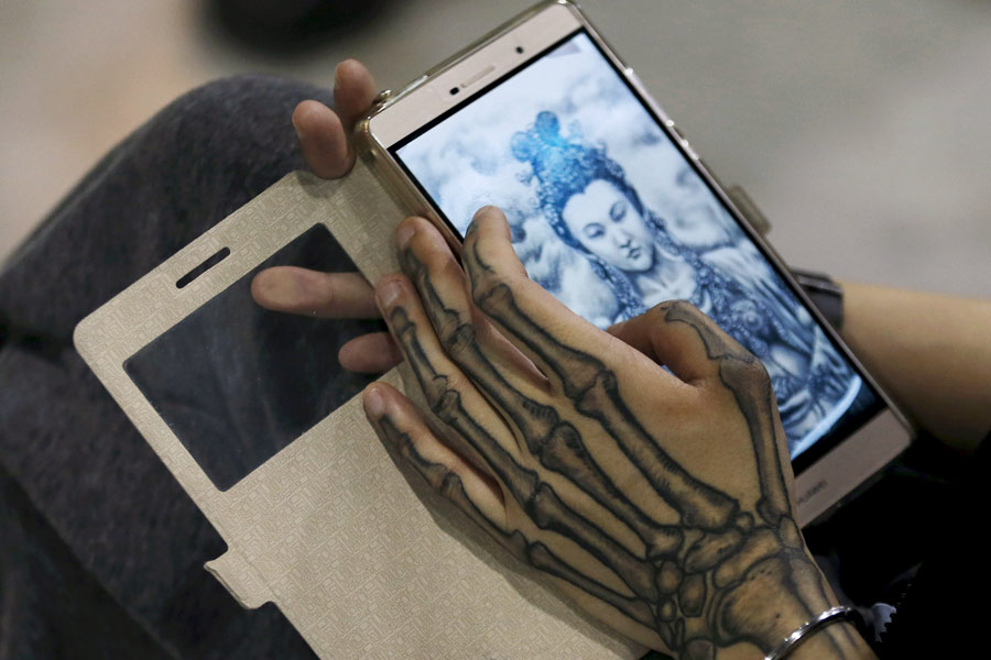 Un artista comprueba una imagen de Buda en su teléfono móvil durante el Festival Internacional de los Tatuajes 2016 de Shanghai, el 23 de abril de 2016. [Foto/Agencias]