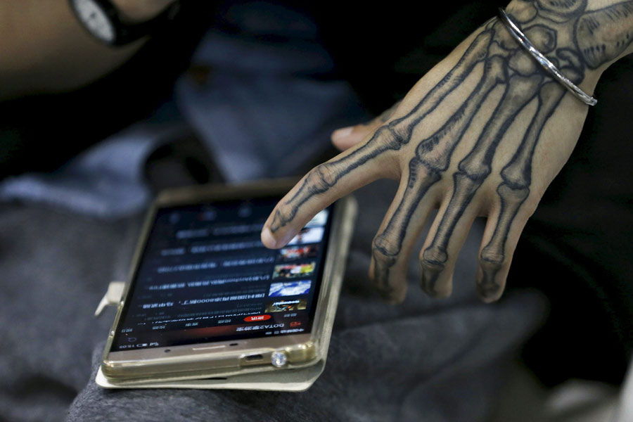 Un artista comprueba su teléfono móvil durante el Festival Internacional de los Tatuajes 2016 de Shanghai, el 23 de abril de 2016. [Foto/Agencias]