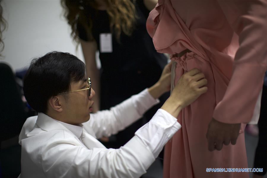 Imagen del 18 de junio de 2016 del diseñador Miao Ran, de China, ajustando la prenda para un modelo previo a su desfile de colección para hombres Primavera/Verano 2016-2017, parte de la Semana de la Moda de Milán, en Milán, Italia. (Xinhua/Jin Yu)