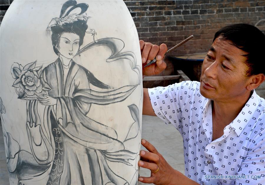 Imagen del 28 de junio de 2016 del artista folclórico Yang Minsheng pintando sobre una obra de porcelana azul y blanca, en la zona turística de Yaotou Kiln en el municipio de Yaotou del condado de Chengcheng, provincia de Shaanxi, en el noroeste de China.El sitio de antiguos hornos populares, cubriendo un área de cuatro kilómetros cuadrados, tiene una historia de elaboración de productos de cerámica de más de mil años. La técnica de elaboración de cerámica en Yaotou Kiln fue incluida en el Patrimonio Nacional Cultural Intangible en el 2006. (Xinhua/Tao Ming)