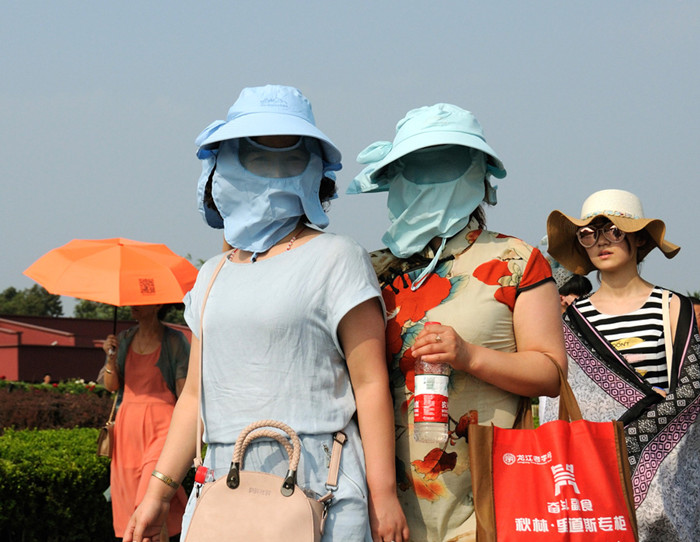 Turistas se cubren la cara para evitar los rayos del sol, el 10 de julio de 2016. [Foto/VCG]