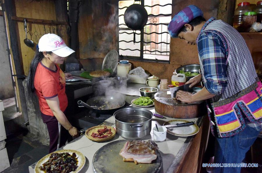 Imagen del 26 de mayo de 2017, de Yu Wulin (d) y su esposa Lu Binghua (i) cocinando la cena para los huéspedes en su estancia familiar en el poblado de Laomudeng en el municipio étnico de Pihe Nu, en la provincia de Yunnan, en el suroeste de China. En 1996, Yu Wulin fue elegido para promover la cultura del grupo étnico Nu en Shanghai y se enamoró de la bailarina Lu Binghua. Después de regresar a su ciudad natal, se casaron y abrieron una estancia familiar para turistas. Crearon una marca de té y vendieron sus productos locales de té a mercados extranjeros. Gracias a la inspiración de la pareja, muchos residentes locales abrieron estancias familiares, y la vida ha cambiado en el poblado remoto. (Xinhua/Yang Zongyou)