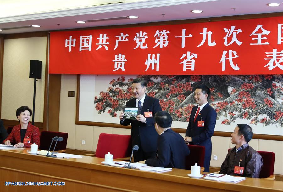 Xi Jinping elogia una fotografía del hermoso paisaje de la aldea de Huamao de la provincia de Guizhou cuando la recibe de manos de Pan Kegang, secretario del Partido de la aldea, durante un panel de deliberación con delegados de Guizhou en el XIX Congreso Nacional del Partido Comunista de China (PCCh), en Beijing, capital de China, el 19 de octubre de 2017. (Xinhua/Lan Hongguang)