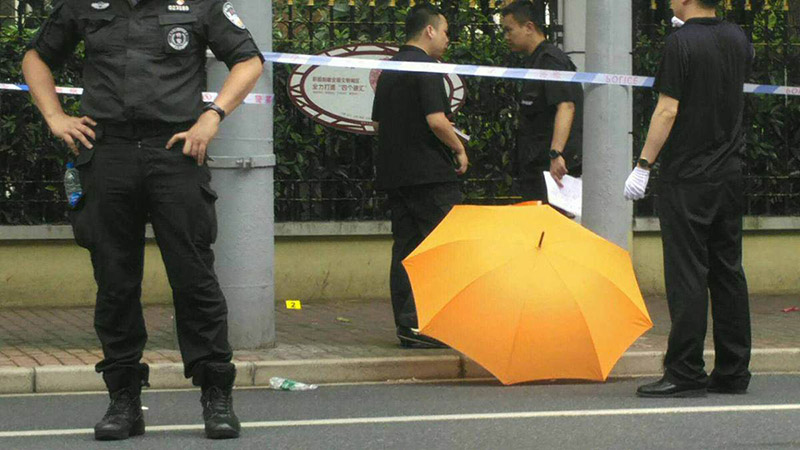 La policía cubre con paraguas la sangre en la escena del ataque con cuchillo ocurrido en Shanghai. [Foto: Gao Erqiang]. 