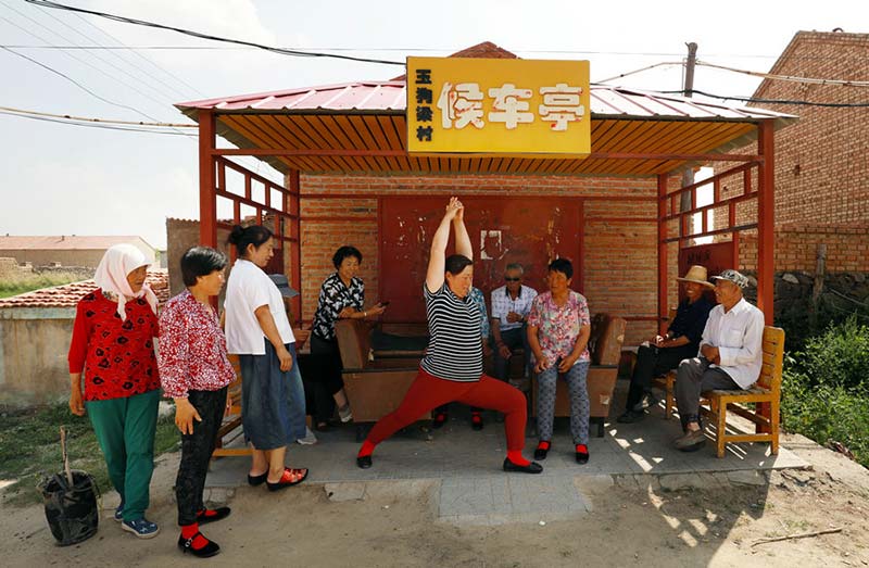 Residentes enseñan habilidades del "Yoga de Yugouliang" mientras esperan el autobús. [Foto: Zhu Xingxin/China Daily]