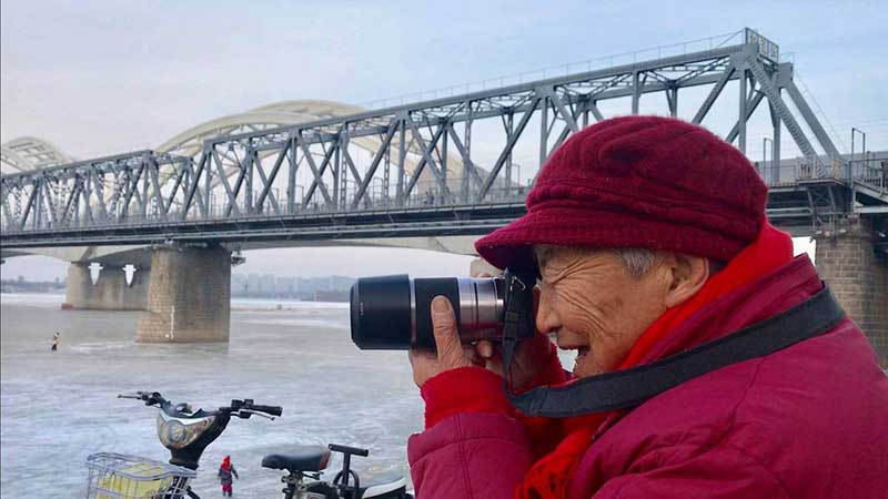 Zhang Ying, de 93 años, toma fotos con su mini cámara digital a la orilla del río Songhua en Harbin, capital de la provincia de Heilongjiang, 14 de diciembre del 2018. [Foto: Wang Kun/ Chinadaily.com.cn]