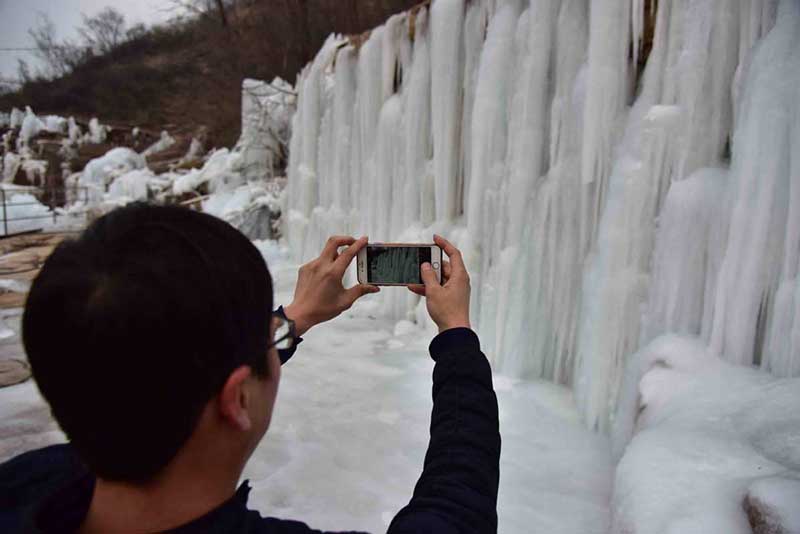 Un turista toma fotos de una cascada congelada en la montaña Wuzhishan de Handan, provincia de Hebei, 15 de enero del 2019. [Foto: Yang Yanzhong/ Chinadaily.com.cn]