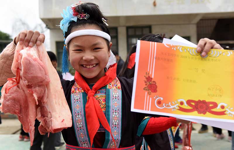 Una estudiante muestra un trozo de carne de cerdo y un certificado obtenido por su buen desempeño académico-en una escuela primaria de Liuzhou, Región Autónoma Guangxi Zhuang. [Foto: Gong Pukang/ Chinadaily.com.cn]