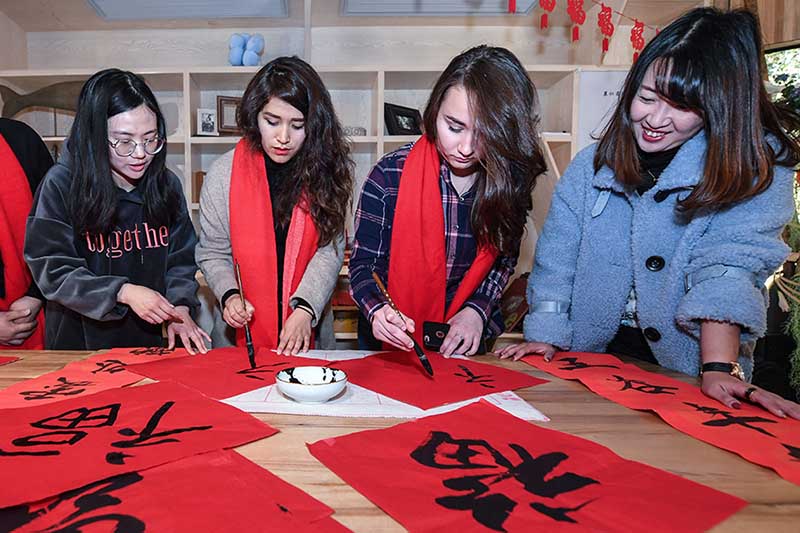 El propietario (a la izquierda) de un hogar que ofrece una habitación en alquiler enseña caligrafía china a sus huéspedes extranjeros, Hangzhou, provincia de Zhejiang. [Foto: Xinhua]