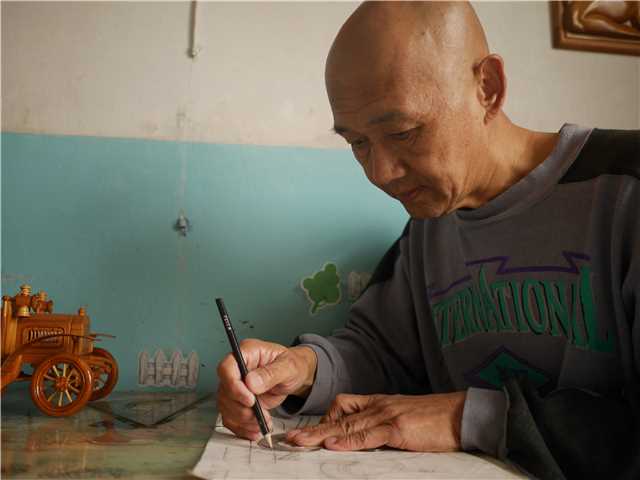 Chuai Mige dibuja un diseño antes de crear la talla en madera. [Foto por Ding Luyang / chinadaily.com.cn]