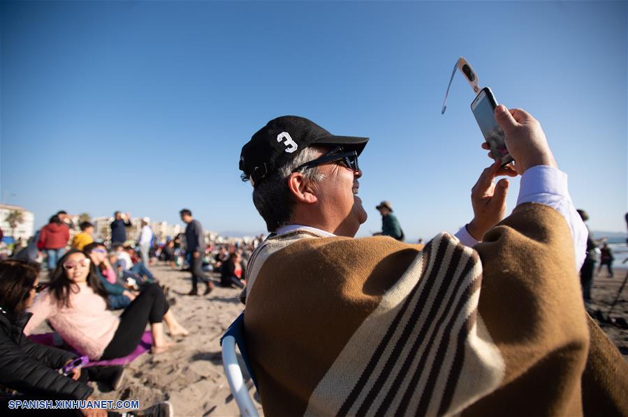 Un hombre observa el eclipse solar total a través de su teléfono móvil, en la ciudad de La Serena, en la región de Coquimbo, Chile, el 2 de julio de 2019. Miles de personas se aglutinaron en las playas de La Serena y Coquimbo, unos 470 kilómetros al norte de Santiago y a nivel del mar, donde el punto central del eclipse solar total tuvo una duración de dos minutos y 15 segundos. (Xinhua/Jorge Villegas)