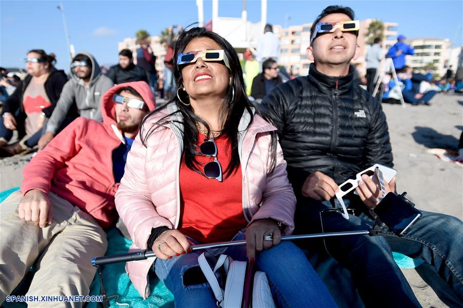 Personas portan lentes para observar el eclipse solar total, en la ciudad de La Serena, en la región de Coquimbo, Chile, el 2 de julio de 2019. Miles de personas se aglutinaron en las playas de La Serena y Coquimbo, unos 470 kilómetros al norte de Santiago y a nivel del mar, donde el punto central del eclipse solar total tuvo una duración de dos minutos y 15 segundos. (Xinhua/Jorge Villegas)