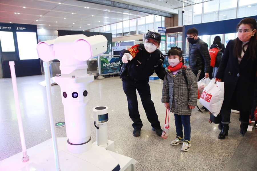 Un policía ayuda a una niña a tomarse la temperatura corporal a través de un robot multifunción en la estación de tren norte de Xi'an, capital de la provincia de Shaanxi, noroeste de China, el 7 de febrero de 2020. (Foto de Zhang Xin / Pueblo en Línea)