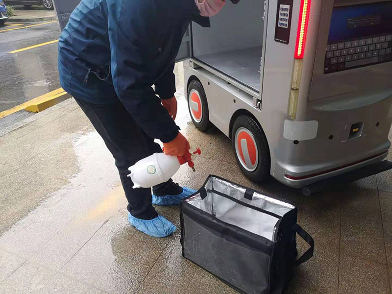 Antes de ponerla en el vehículo no tripulado, un trabajador desinfecta una caja donde depositará la comida solicitada. [Foto: proporcionada a chinadaily] 