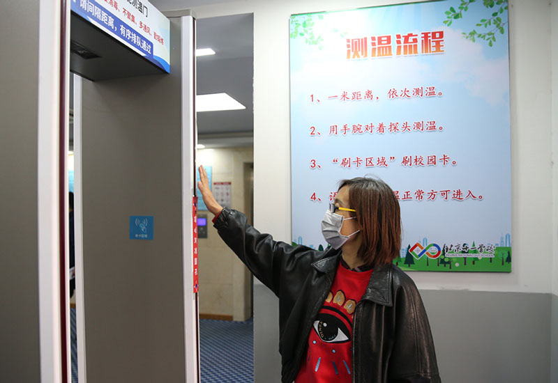 Una empleada instala un arco de monitoreo de temperatura en la entrada de un dormitorio de estudiantes en la Escuela del Día Nacional de Beijing, el 21 de abril de 2020. [Foto de Zuo Hong / chinadaily.com.cn]