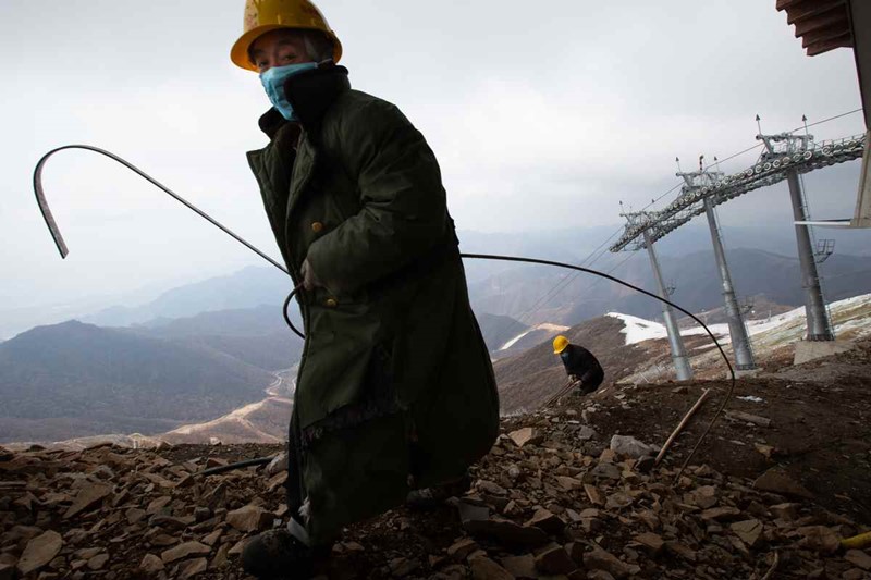 Los trabajadores vestidos con gruesos abrigos limpian los escombros en el sitio de construcción del Centro Nacional de Esquí Alpino en la montaña Haituo de Yanqing en Beijing el 17 de abril. [Foto de Kuang Linhua / China Daily]
