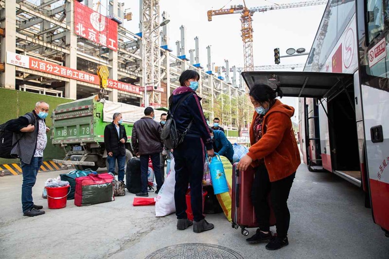 Los trabajadores migrantes de la provincia de Sichuan llegan al sitio de construcción del Centro Nacional de Convenciones en un autobús alquilado el 16 de abril. Para reducir el riesgo de infecciones en los viajes, unos autobuses habilitados transportan a los trabajadores migrantes desde sus lugares de origen hasta los sitios de construcción. [Foto por Kuang Linhua / China Daily]