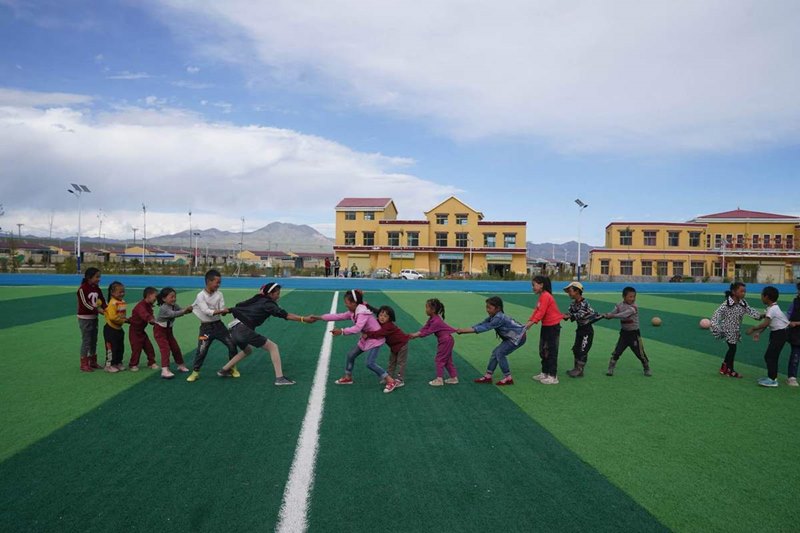 Niños juegan en un campo de fútbol en la Aldea Cultural Amdo, un proyecto de reasentamiento para familias pobres en el condado Xinghai, provincia de Qinghai. [Foto de Feng Yongbin / China Daily]