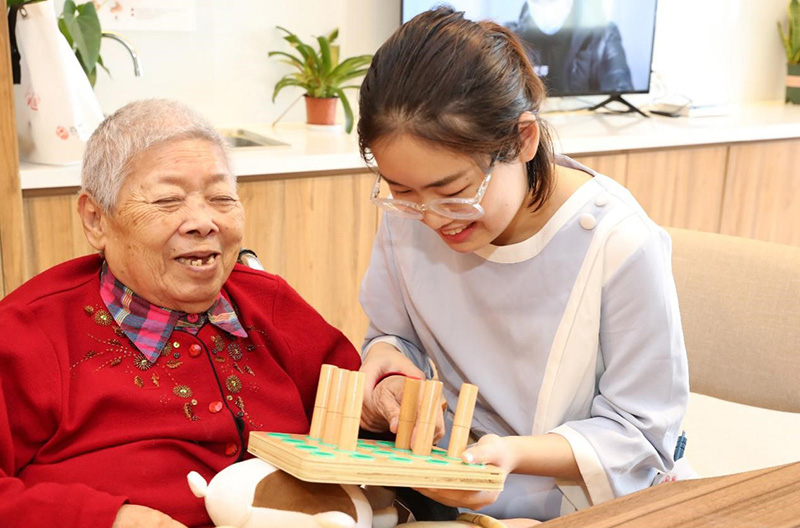 El personal ayuda a una anciana con movilidad reducida a hacer ejercicios de recuperación con bloques de madera para fortalecer la capacidad de agarre de sus dedos en un centro de salud en Nantong, provincia de Jiangsu, en el este de China. (Xu Congjun / Pueblo en Línea)
