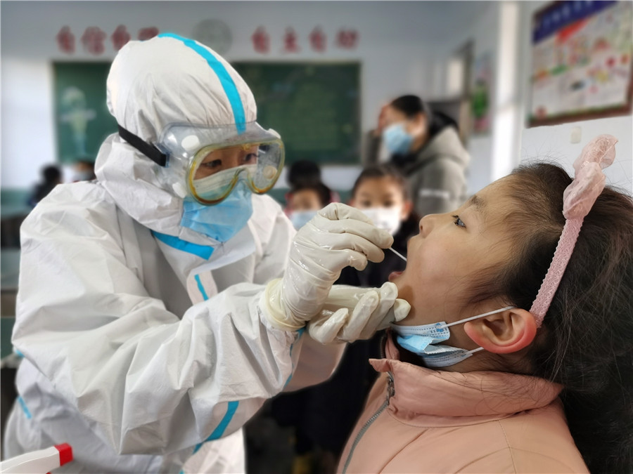 Un trabajador médico toma una muestra de garganta de una estudiante en una escuela primaria en Xingtai, provincia de Hebei, el 6 de enero de 2021. La ciudad lanzó una campaña masiva de pruebas de ácido nucleico gratuitas después de un reciente brote de COVID-19. [Foto de Huang Tao / para China Daily]