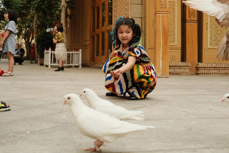 Los niños alimentan a las palomas en Tuancheng, la ruta peatonal más famosa en la ciudad de Hotan, en la región autónoma de Xinjiang, en el noroeste de China, el 22 de mayo de 2021 (Pueblo en Línea / Zhang Ruohan).