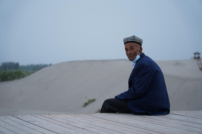Un hombre Uygur se sienta en un caballete de madera en la parte suroeste del desierto de Taklamakan en Hotan, en la región autónoma Uygur de Xinjiang, en el noroeste de China, el 21 de mayo de 2021 (Pueblo en Línea / Zhang Ruohan).