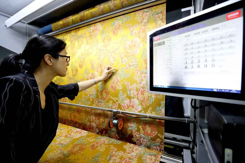 En un taller de inspección inteligente ubicado en el condado de Xinchang, provincia de Zhejiang, un diseñador hace una comprobación final de las telas terminadas, 22 de mayo del 2021. [Foto: Xinhua]