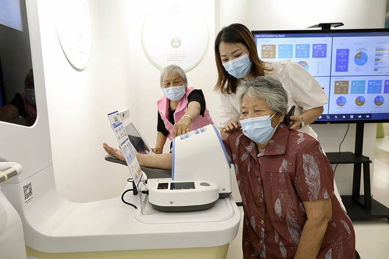 Residentes de la tercera edad comprueban su presión arterial en un área de autoservicio en un centro de salud pública de Yaozhuang, condado de Jiashan, en Jiaxing, provincia de Zhejiang, 13 de julio del 2021. [Foto: Zhu Xingxin/ China Daily]