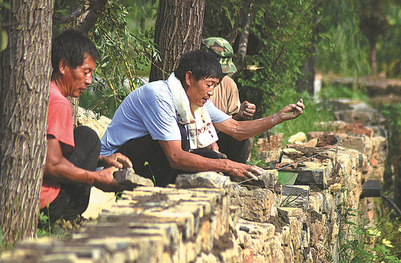 Feng coloca ladrillos para construir un muro con dos aldeanos. [Foto de Zhao Dongshan y Fu Youmin / para China Daily]