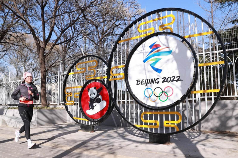 Una aficionada de las carreras pasa por delante de un cartel de los Juegos Olímpicos de Invierno de 2022 con características chinas en una calle de Beijing, el 24 de noviembre de 2021. (Por Chen Xiaogen/Pueblo en Línea)