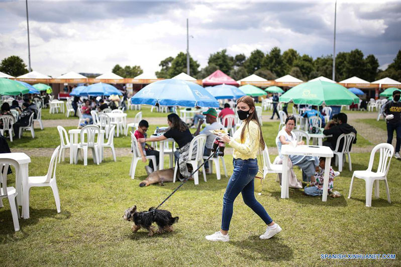 Una mujer pasea a un perro mientras lleva alimentos durante el festival de gastronomía "Alimentarte" en el Parque Simón Bolívar, en Bogotá, Colombia, el 19 de marzo de 2022. El festival de gastronomía más importante en Colombia "Alimentarte" se llevará a cabo por cuatro fines de semana en distintos parques icónicos de la ciudad. (Xinhua/Jhon Paz)