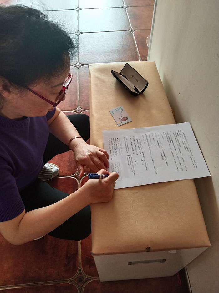 Una anciana, residente en la Zona de Libre Comercio del Puerto de Tianjin, firma el formulario de rigor después de que los voluntarios le explicaron los beneficios y los posibles efectos secundarios de la vacuna contra el COVID-19, 23 de abril del 2022.