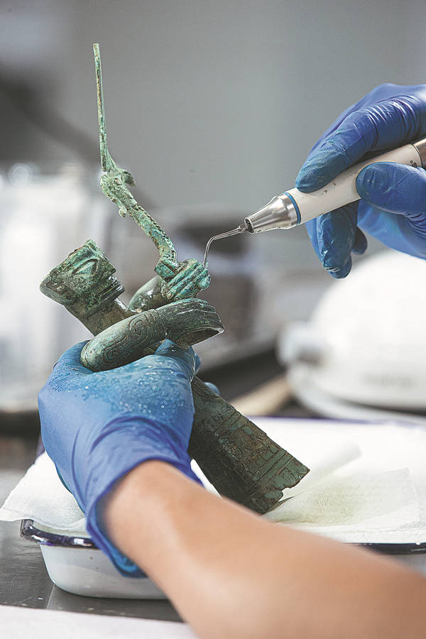 Un arqueólogo utiliza una herramienta especial para limpiar una estatuilla de bronce en el laboratorio del sitio de excavación en Sanxingdui, Guanghan, provincia de Sichuan, 9 de junio del 2022. [Foto: Yu Jia/ China Daily]