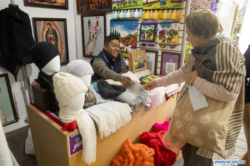 Un artesano muestra sus productos textiles a una mujer durante la Feria Nacional de Artesanía "De Nuestras Manos", en el parque Kennedy de Miraflores, en Lima, Perú, el 17 de agosto de 2022. Con la participación de alrededor de 100 artesanos de todo el país, la feria se lleva a cabo hasta el 21 de agosto. (Xinhua/Mariana Bazo) 
