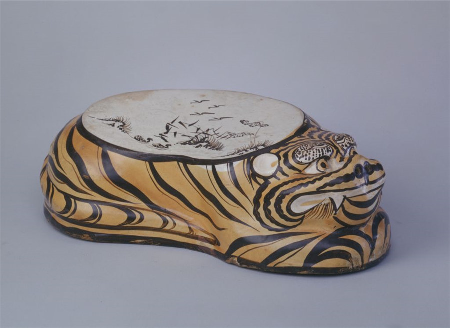 Una almohada pintada en forma de tigre con esmalta marrón. La espalda del tigre sirve como superficie de almohada, con un fondo blanco y una pintura que representa aves de otoño en un pantano de juncos. [Foto: Sitio web oficial del Museo del Palacio Imperial de Beijing]
