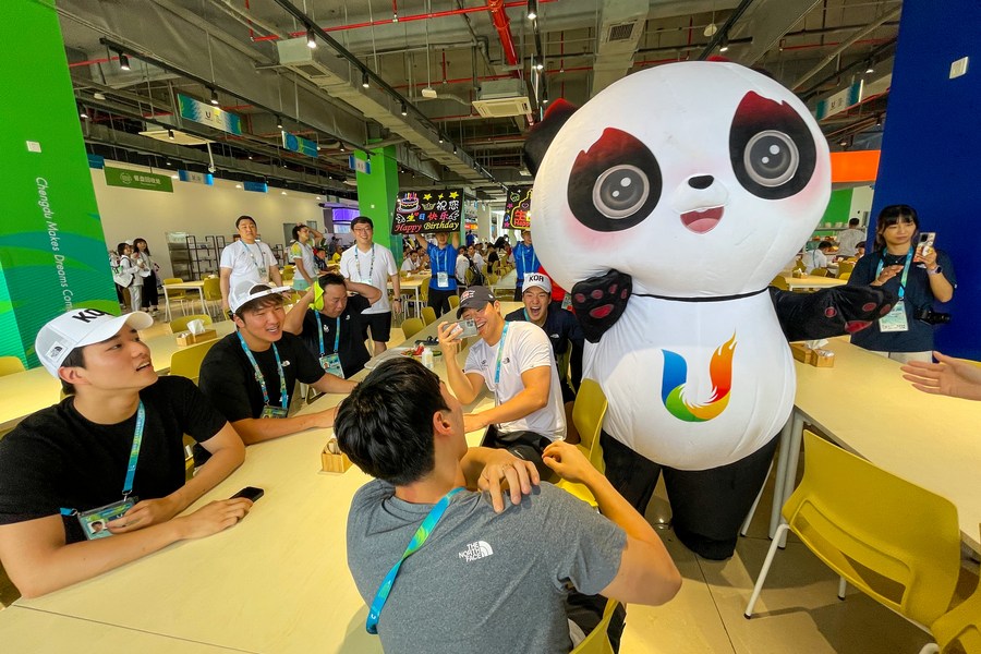 Un empleado del comedor disfrazado de la mascota Rongbao, festeja el cumpleaños de los jugadores de República de Corea en la Villa de la 31ª edición de verano de los Juegos Mundiales Universitarios de la FISU, en Chengdu, en la provincia de Sichuan, en el suroeste de China, el 30 de julio de 2023. (Xinhua/Shen Bohan)