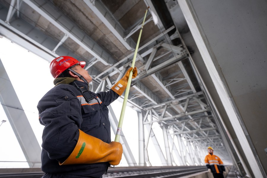  Imagen del 4 de febrero de 2024 de un empleado retirando el hielo que cubre el sistema de catenaria aérea, en el puente Tianxingzhou sobre el río Yangtze, en Wuhan, en la provincia de Hubei, en el centro de China. (Xinhua/Xiao Yijiu)