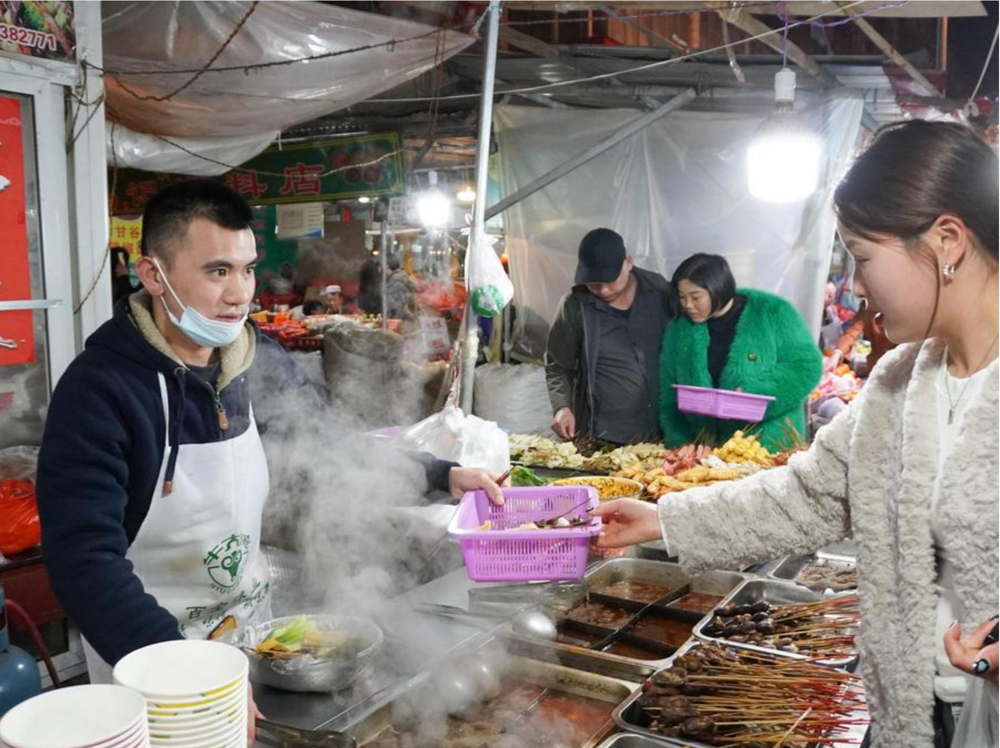 Un propietario de un puesto de sopas "malatang" atiende a una cliente en una calle de locales de comida callejera al paso en el distrito de Qinzhou de la ciudad de Tianshui, provincia de Gansu, en el noroeste de China, el 19 de marzo de 2024. (Xinhua/Ma Xiping)