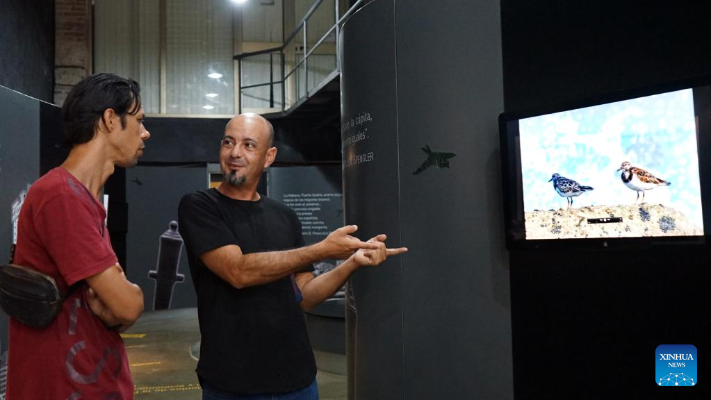 El geógrafo cubano, Adrián Espinosa (d), conversa con un visitante en la exposición de fotografía de naturaleza "Paraísos susceptibles: Cuba", en La Habana, capital de Cuba, el 5 de julio de 2024. (Xinhua/Li Zijian)