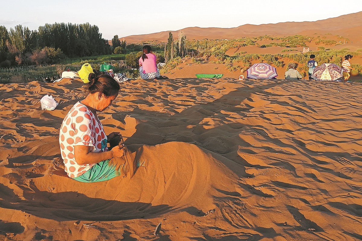 Los turistas prueban la terapia con arena en el condado Shanshan, región autónoma Uygur de Xinjiang, en julio. [Foto proporcionada a China Daily]