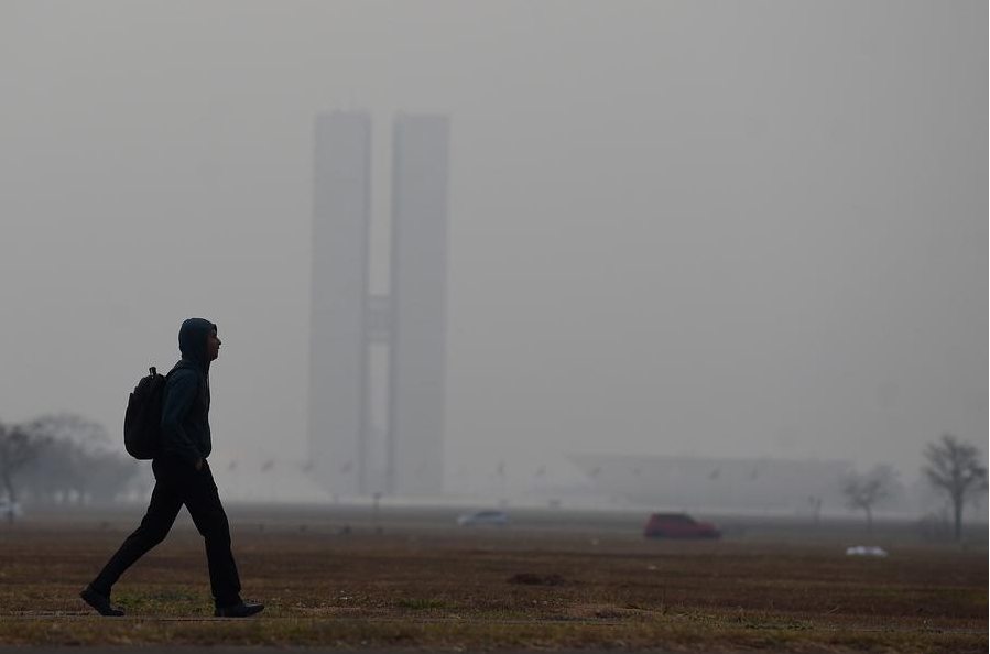 Un hombre camina por una calle mientras la sede del Congreso Nacional permanece cubierta con el humo provocado por los incendios forestales durante la temporada de clima seco, en Brasilia, Brasil, el 26 de agosto de 2024. (Xinhua/Lucio Tavora) 