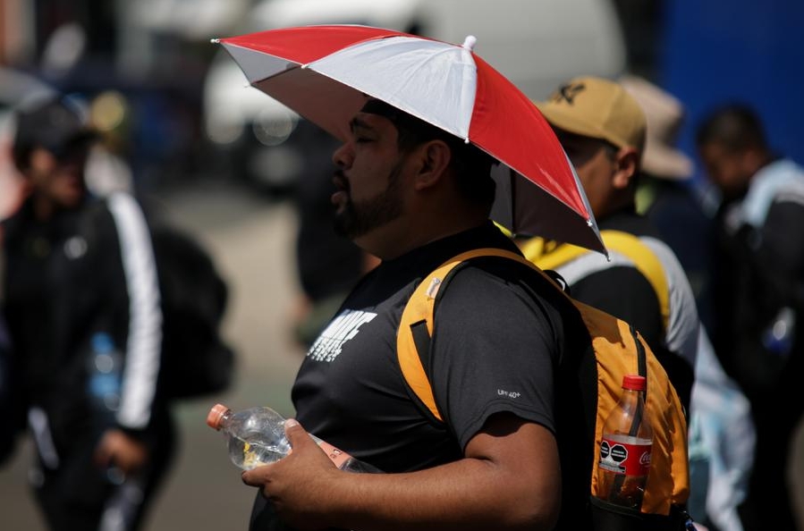 Imagen del 22 de febrero de 2024 de un hombre cubriéndose del sol mientras camina por una calle durante una ola de calor, en la Ciudad de México, capital de México. (Xinhua/Francisco Cañedo) 
