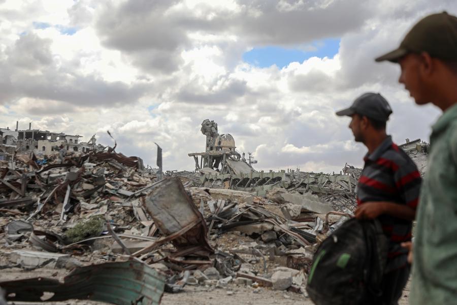 Imagen del 12 de octubre de 2025 de palestinos caminando frente a los escombros de edificios destruidos después de regresar a Khan Younis, en el sur de la Franja de Gaza. (Xinhua/Rizek Abdeljawad) 