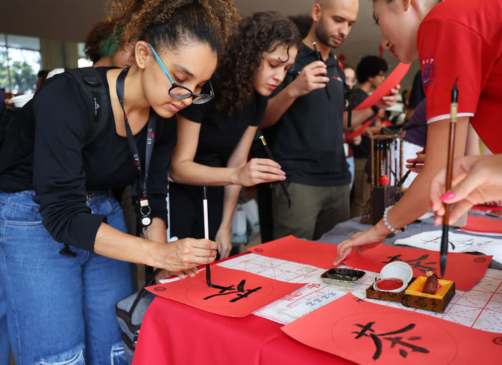 Estudiantes brasileños experimentan la caligrafía china durante el acto inaugural de la exposición itinerante "Sabores que cruzan océanos y montañas: la ruta del té y la ruta del café", celebrado en la Universidad Federal de Minas Gerais, en la ciudad brasileña de Belo Horizonte, el 22 de abril de 2026. (Xinhua/Jin Haoyuan)