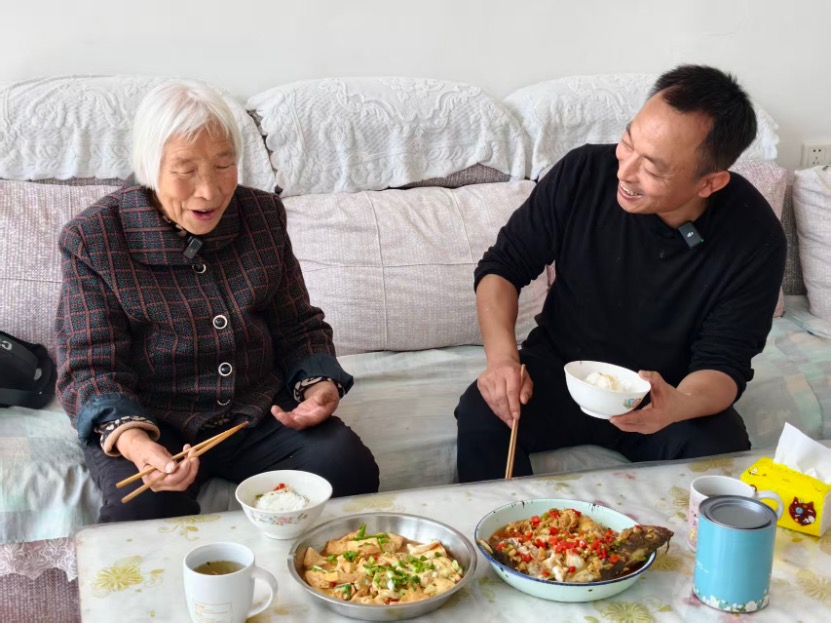 Li Quansheng (derecha), primer secretario del Partido de la aldea de Dongshaoqu —en el municipio homónimo del distrito de Miyun, Beijing—, comparte una comida con una anciana de la localidad. (Diario del Pueblo digital/Chang Sha)