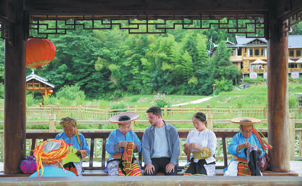 Un turista extranjero observa a mujeres del grupo étnico Yao crear bordados de punto de cruz en el condado Longhui, en Shaoyang, provincia de Hunan, 4 de agosto del 2026. [Foto: Xinhua]